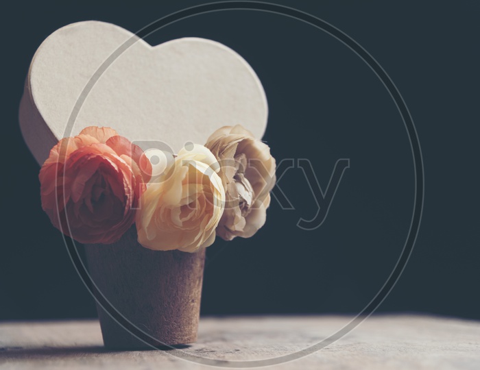 Close up of Heart shaped card with rose flowers in a wooden cup with black background