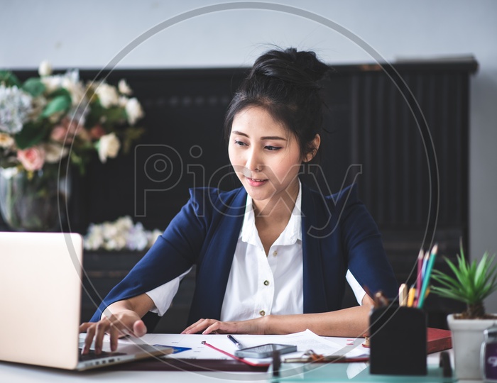 Portrait of smiling pretty young Asian businesswoman working on Laptop at Office