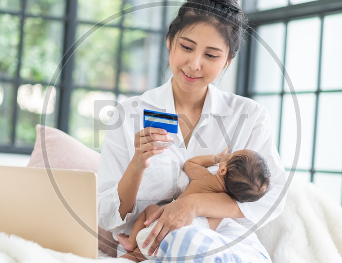 Asian Mother taking care of her baby while working online