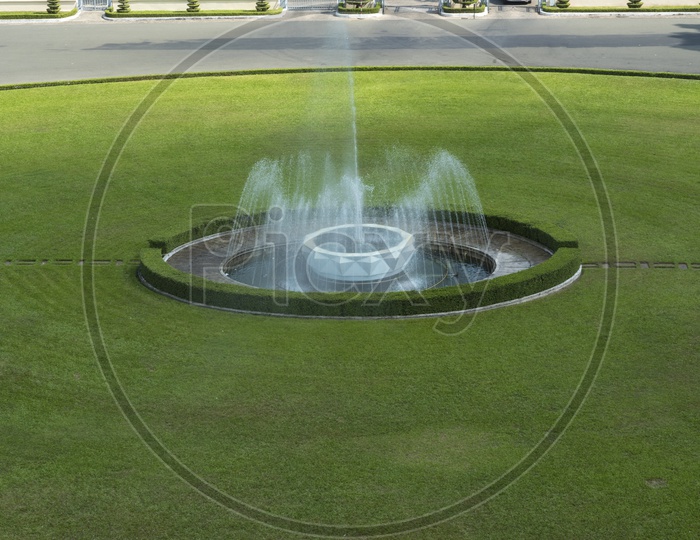 A large fountain in the middle of a green lawn.