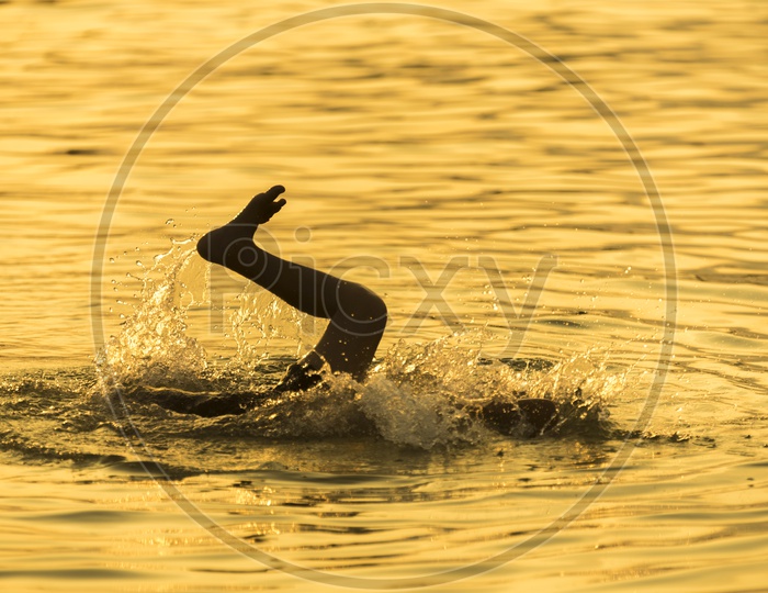 Silhouettes of Child Swimming in Lake over Sunlight
