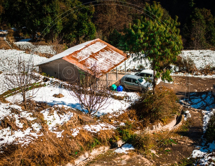 A Small House Covered in Snow with Cars Parked Outside