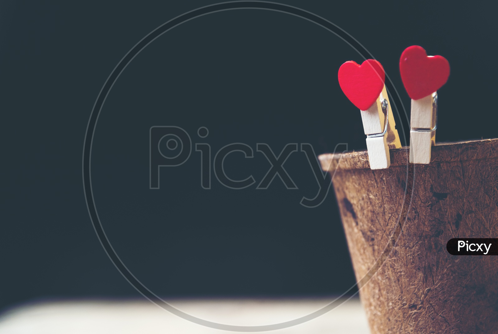Heart shaped wooden clips holding a wooden cup with black background