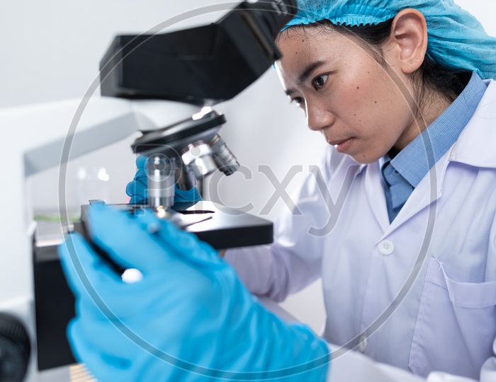 Asian Female Scientist or Medical Student Analyzing Sample through Microscope