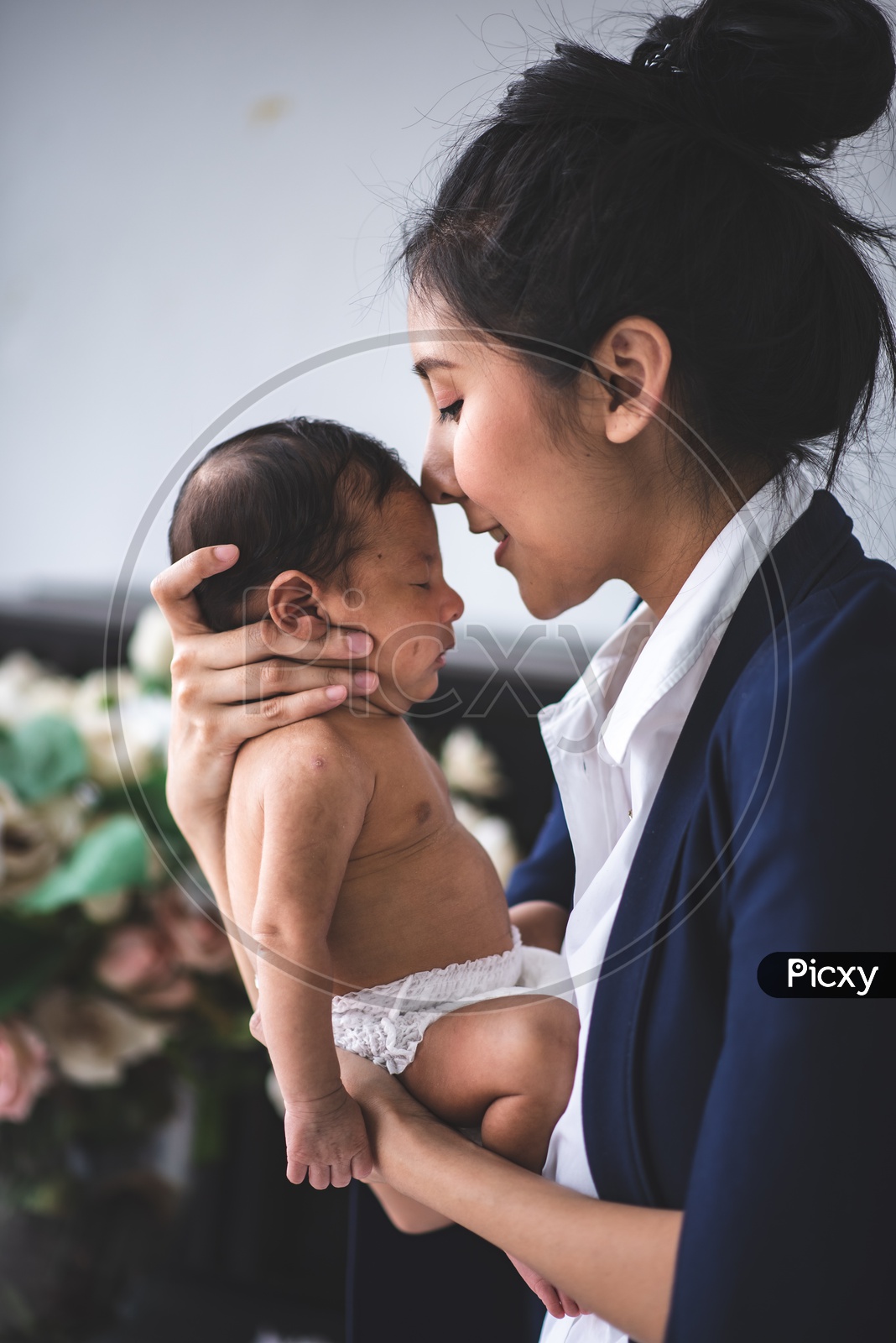 Young Asian Mother Kissing her newborn Baby while doing office work