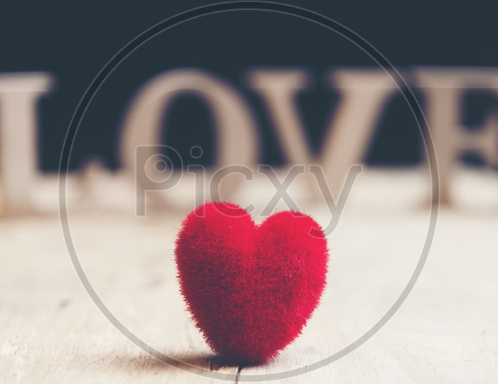 A soft fur heart shaped toy in focus and wooden letters forming word LOVE in the background