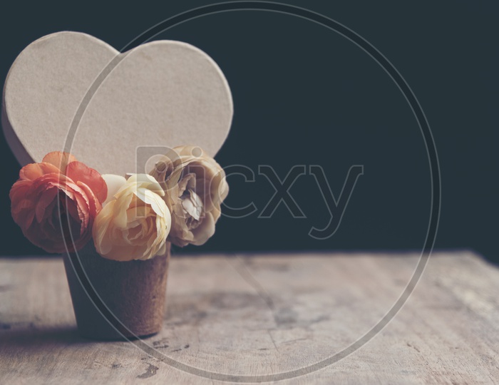 Heart shaped card with rose flowers in a wooden cup with black background