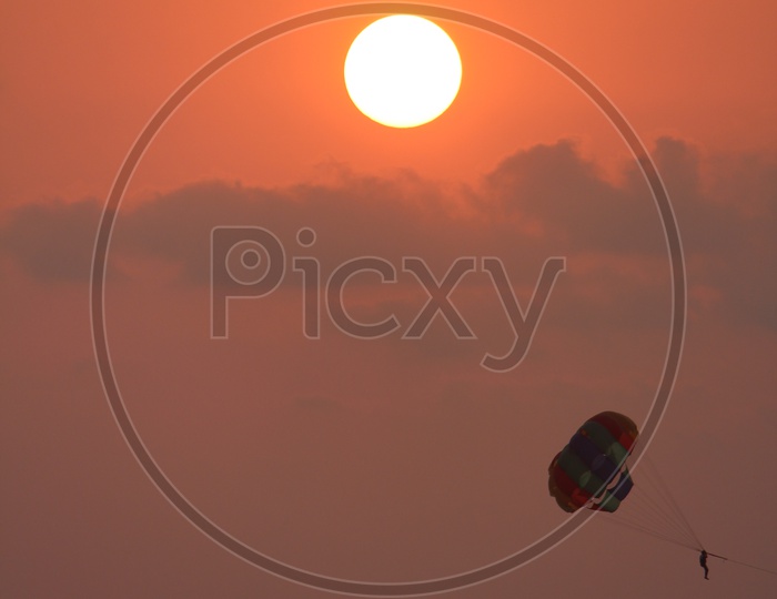 Paragliding Over Sea In Goa With Bright Round Sun in Background