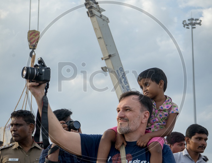 A man with a small child on shoulder and capturing images at nimarjan