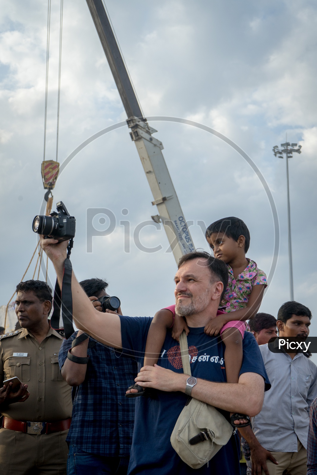 A man with a small child on shoulder and capturing images at nimarjan