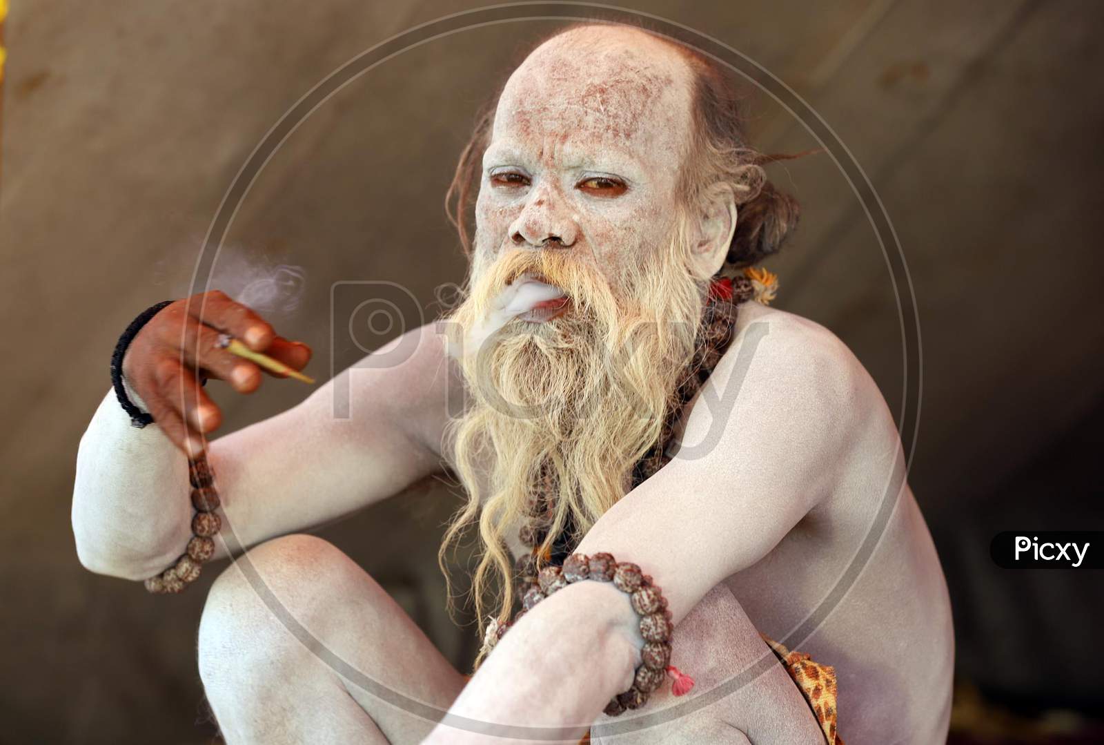 A Naga Sadhu Or Holy Man Apply Ashes On His Body Smoking Bidi On A Cold And Fogy Weather At An Akhada Camp At Kumbh Mela In Prayagraj, January 8, 2019.