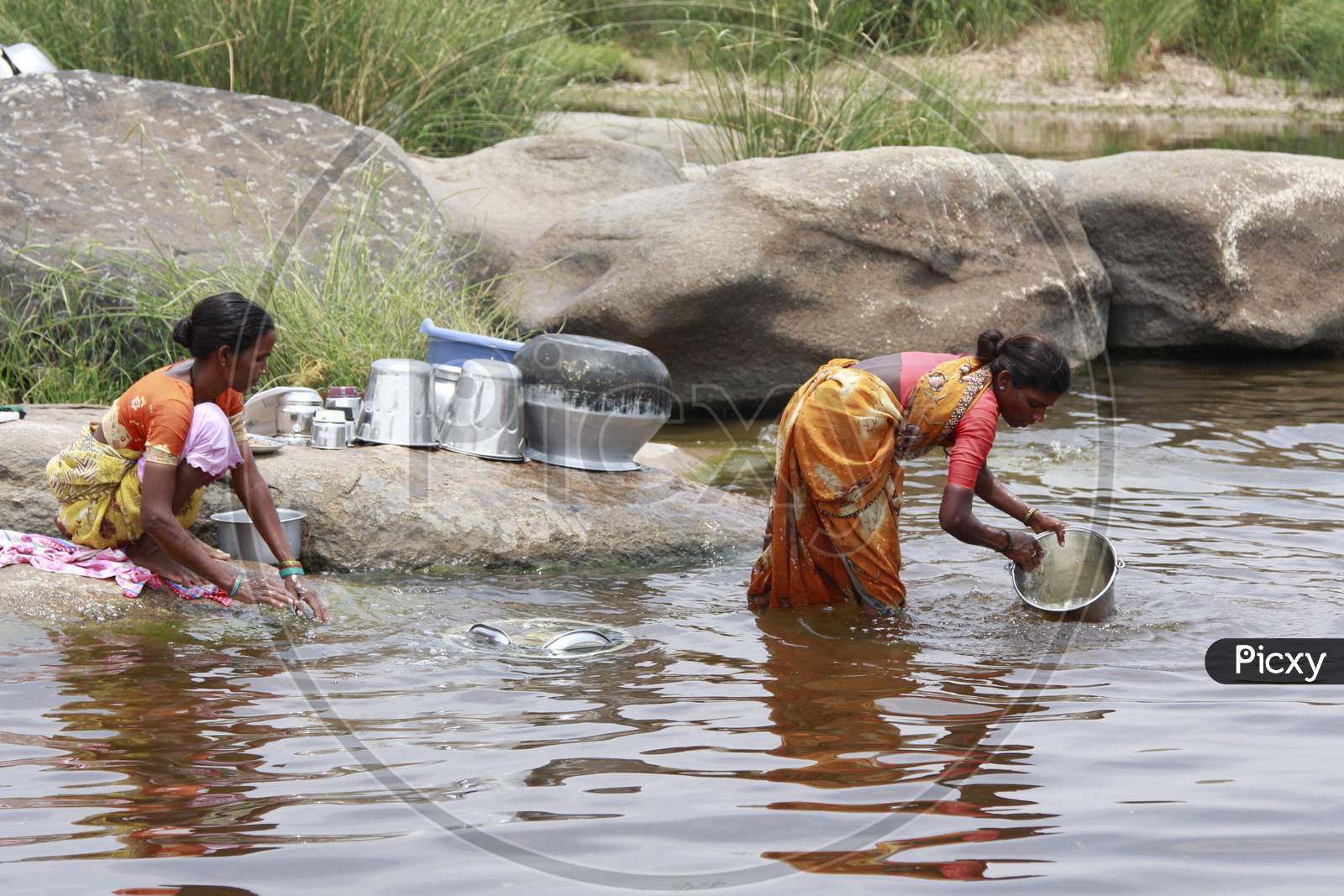 Indian Women washing dishes by the pond