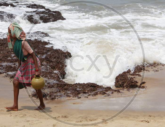 A Woman carrying water in a pot by the beach