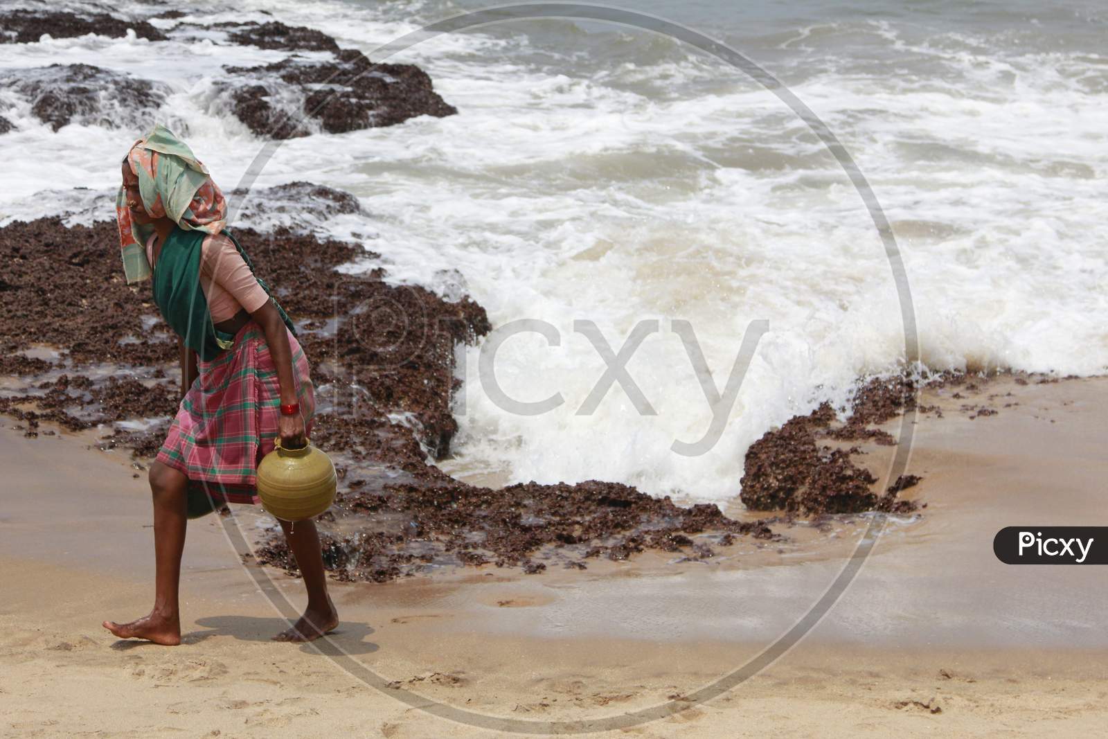A Woman carrying water in a pot by the beach
