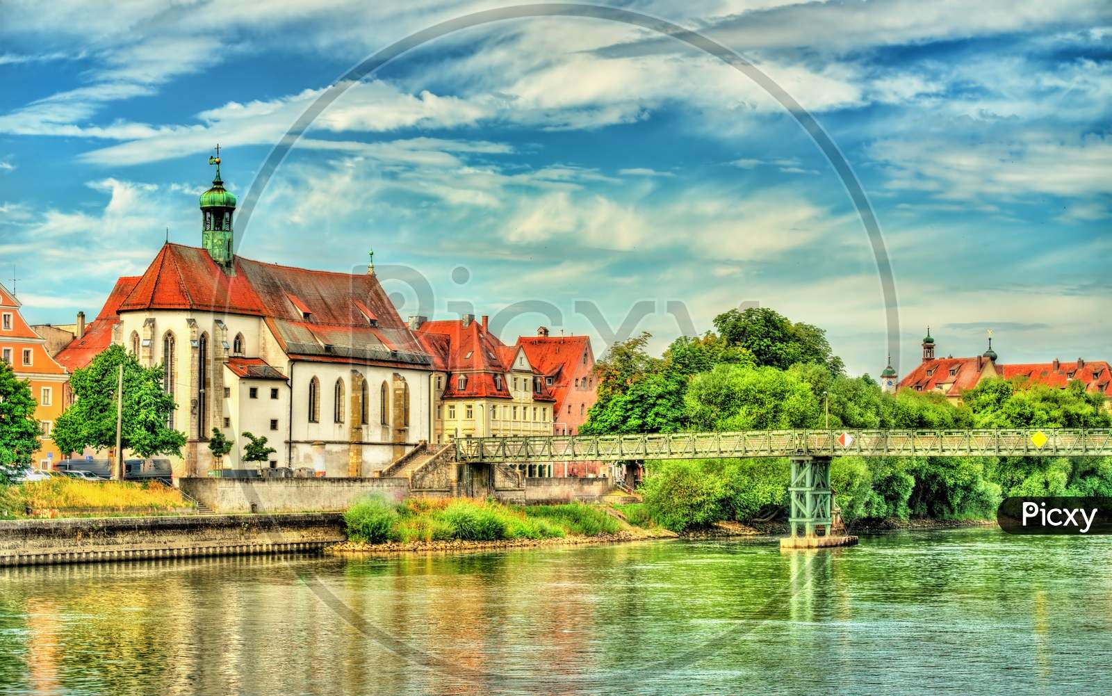 St. Oswald Church With Eiserner Steg Bridge Across The Danube River In Regensburg, Germany