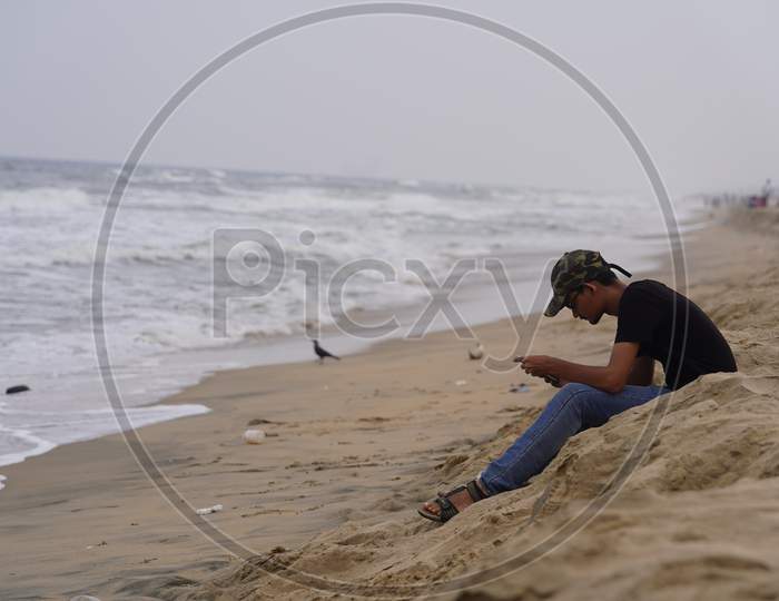 Young Man Using Smart Phone by Sitting On a Beach Sand