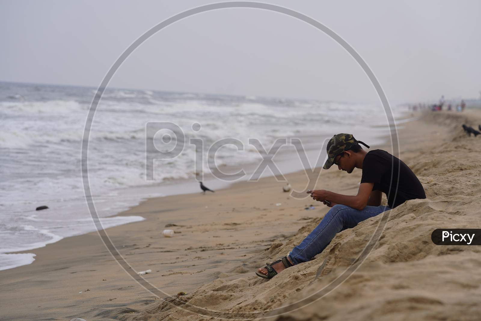 Young Man Using Smart Phone by Sitting On a Beach Sand