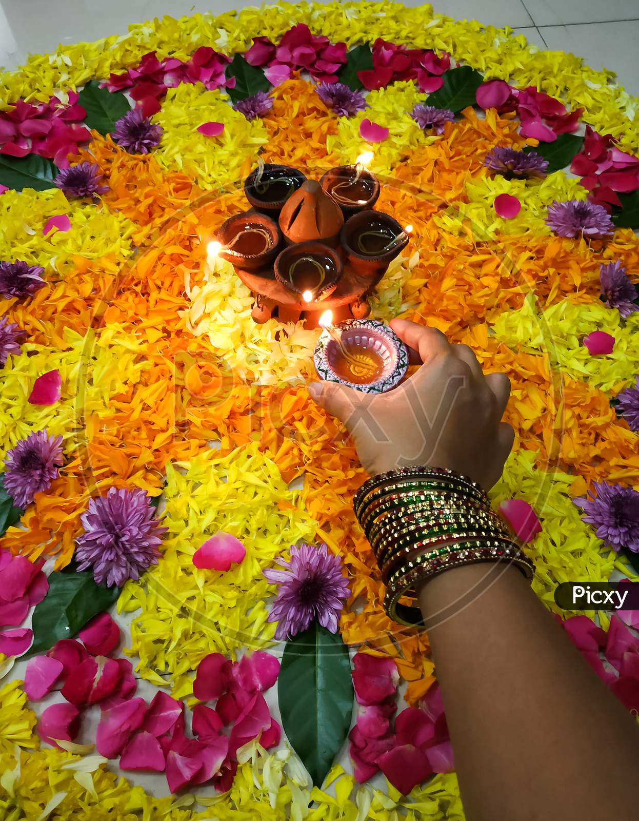 Hand of a women with bangles liting a diya in the flower rangoli