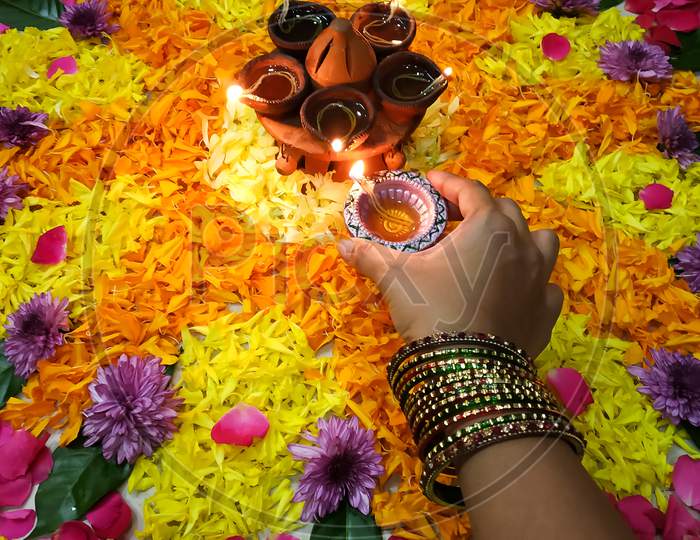Hand of a women with bangles liting a diya in the flower rangoli