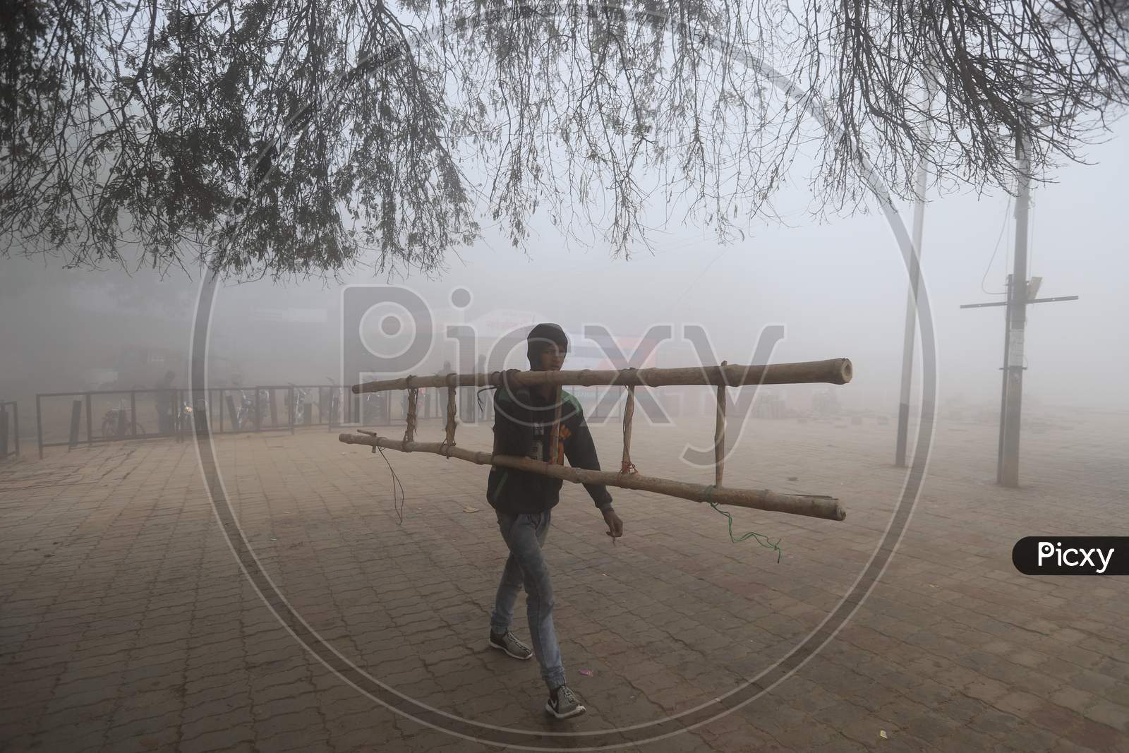 A Man Carrying A Ladder In Morning Mist