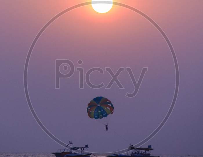 Tourists Enjoying Paragliding Over Sea In  Vizag  With Bright Sun In Background