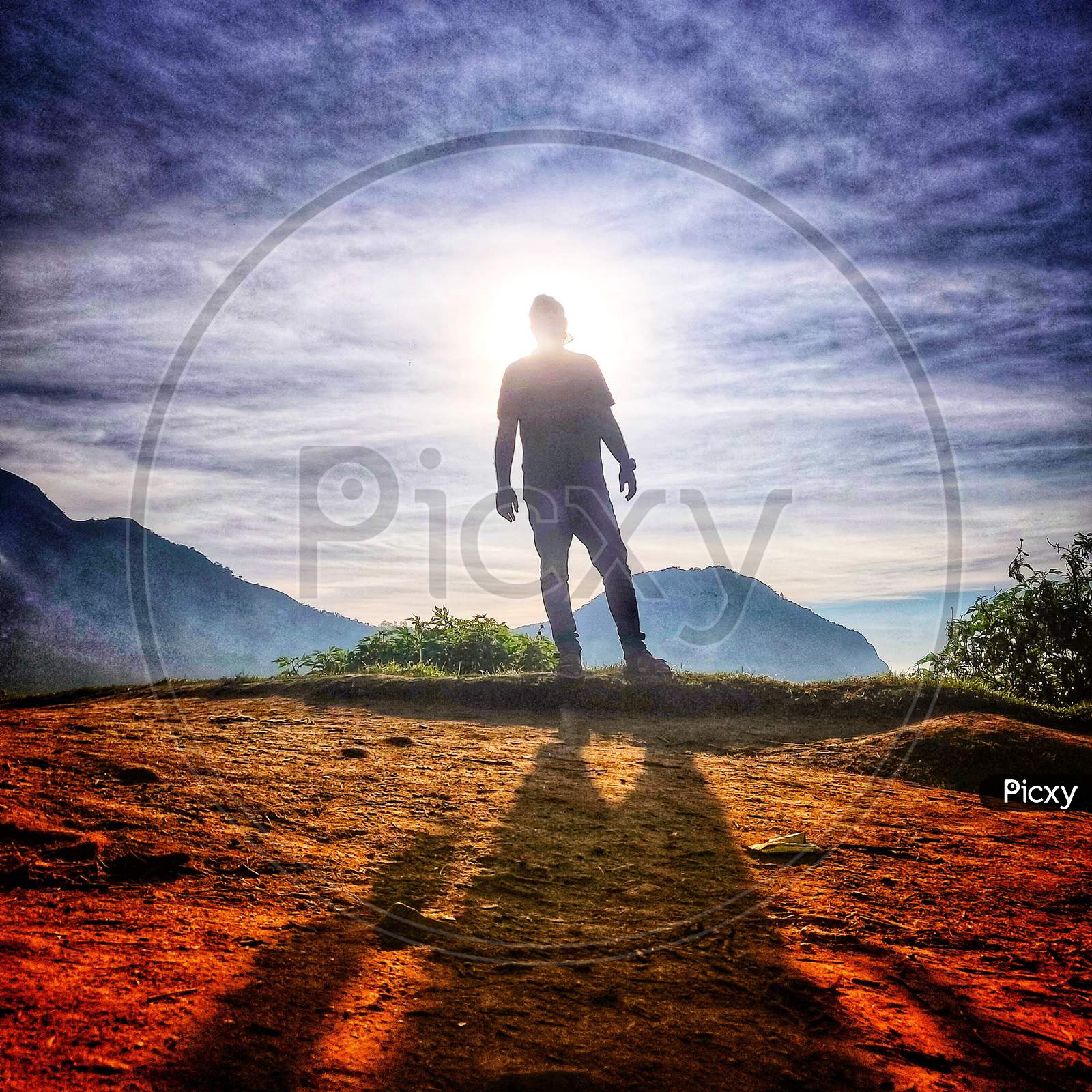 Silhouette Of Man Standing At a Terrain Cliff With Bright Sun In Background