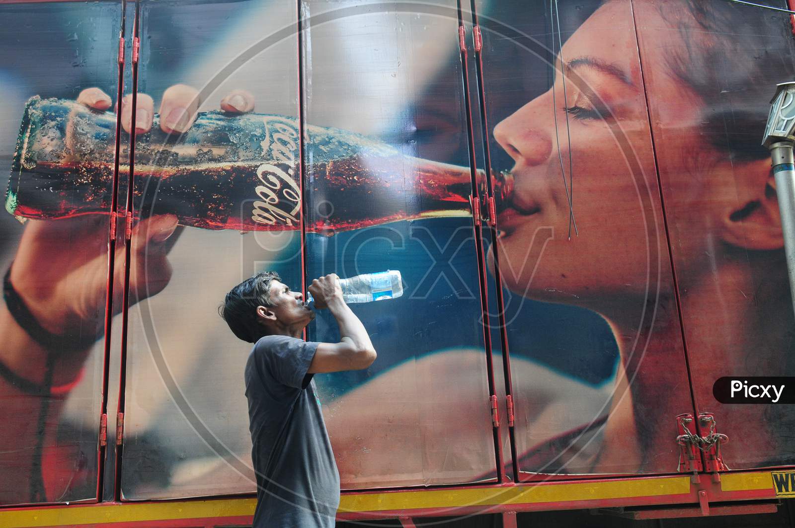 Indian man drinking water alongside a poster of coco cola