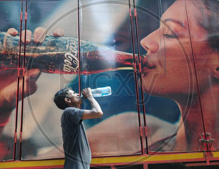 Indian man drinking water alongside a poster of coco cola