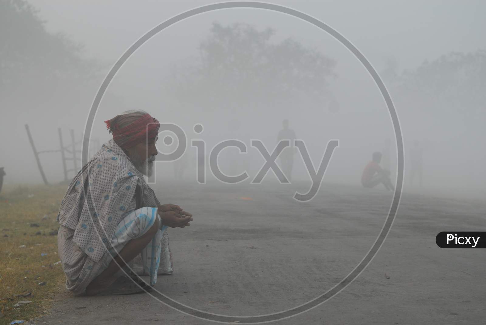 Indian Old man sitting by the road during a foggy morning