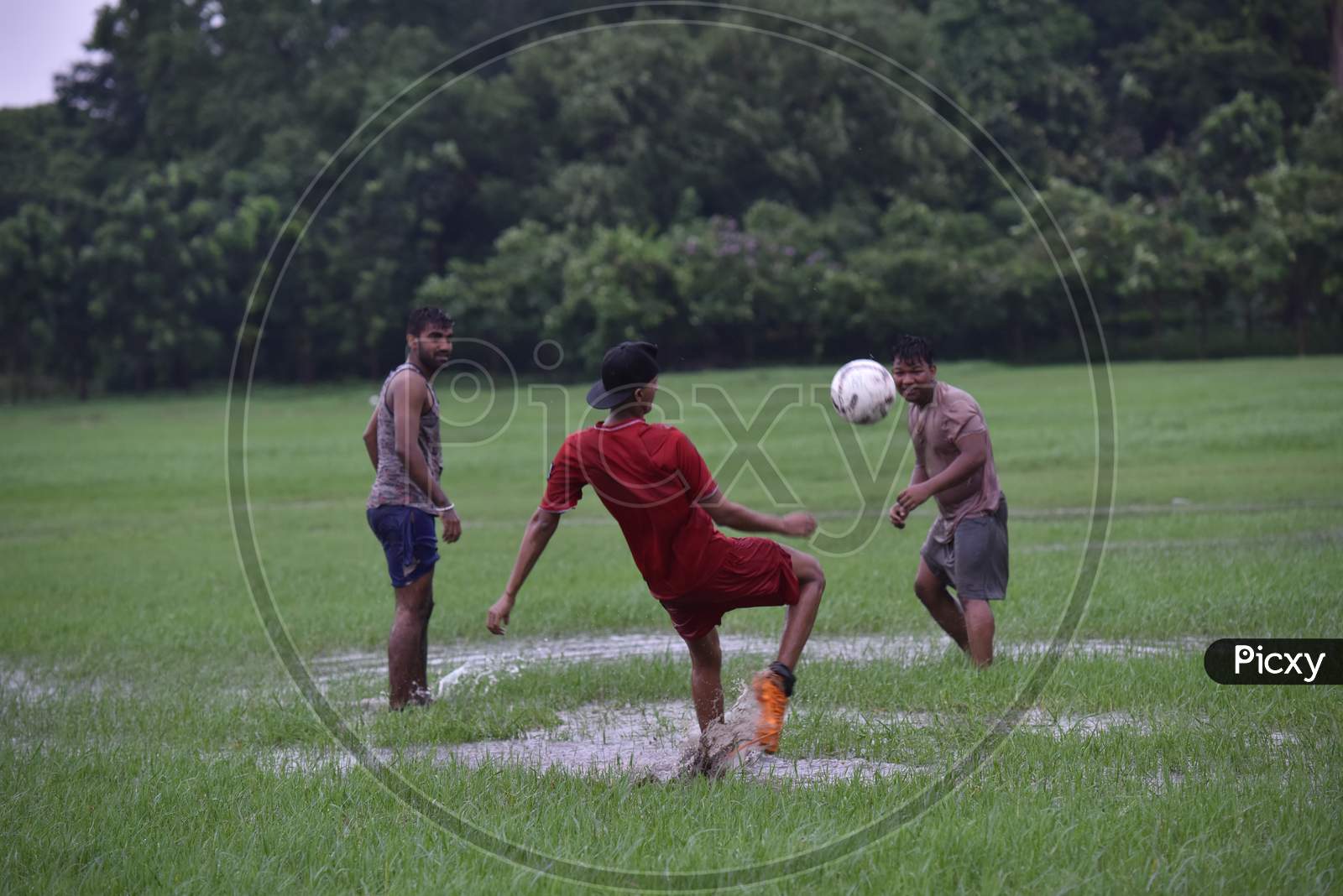 Indian boy attempting a football kick during rain