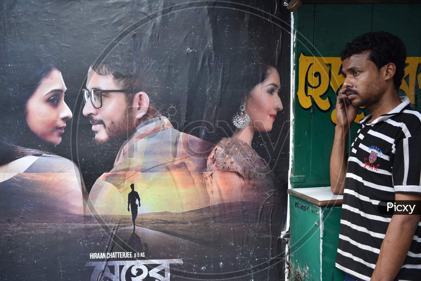 Indian man speaking on the phone alongside movie poster