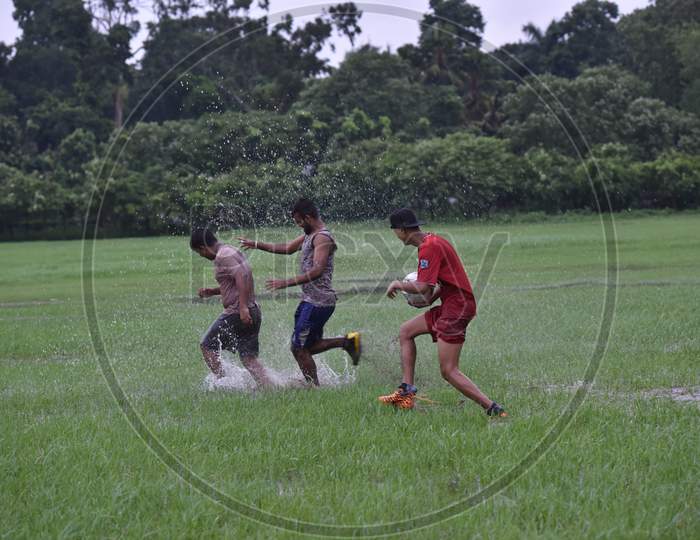 Three Indian boys playing with football in the rain