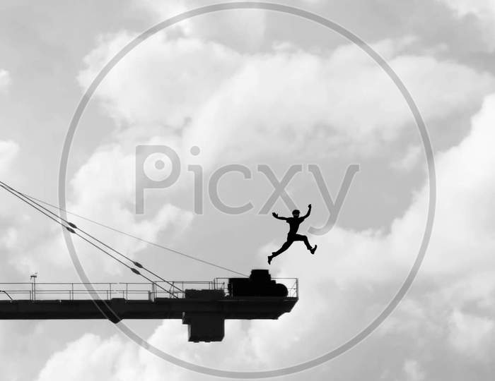 Silhouette of an Man Jumping From an Construction Crane With Clouds In Background