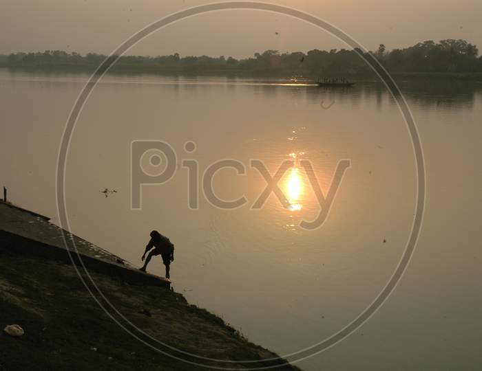 A Man washing his legs by the river during sunset