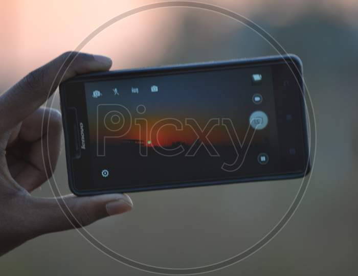 Man Capturing Sunset in Smartphone