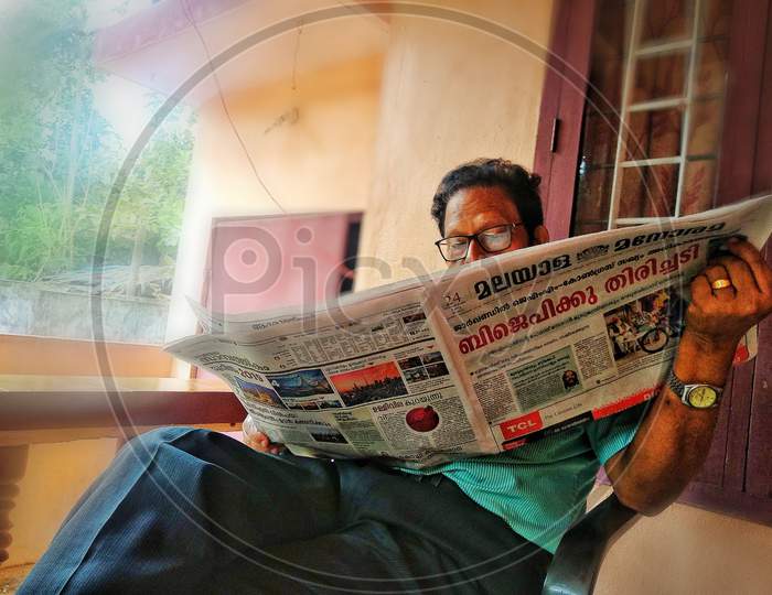 A Man Reading Malayalam Daily Newspaper By Sitting in a House