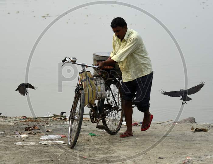 Fish Vendor Cleans His Bicycle And Basket After Selling His Catch On The Banks Of The River Brahmaputra In Guwahati