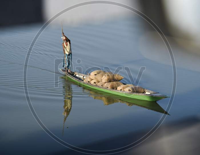 Indian Man Paddle A Boat In A Lake Loaded With Rice Grain Bags, To Sell In The Nearest Market, At Kayakuchi Village In Barpeta District Of Assam