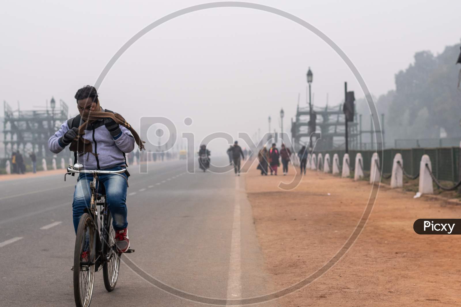 A man wearing muffler and other winter wears and riding bicycle in the foggy evening during winters in Delhi NCR