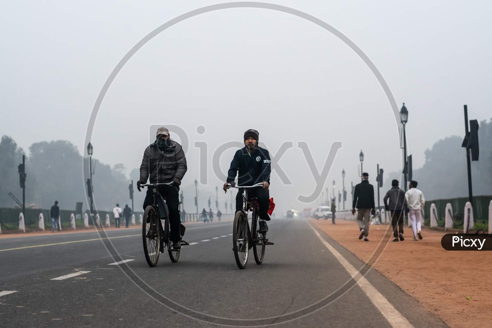 Two men wearing winter wears and riding bicycle in the foggy evening during winters in Delhi NCR