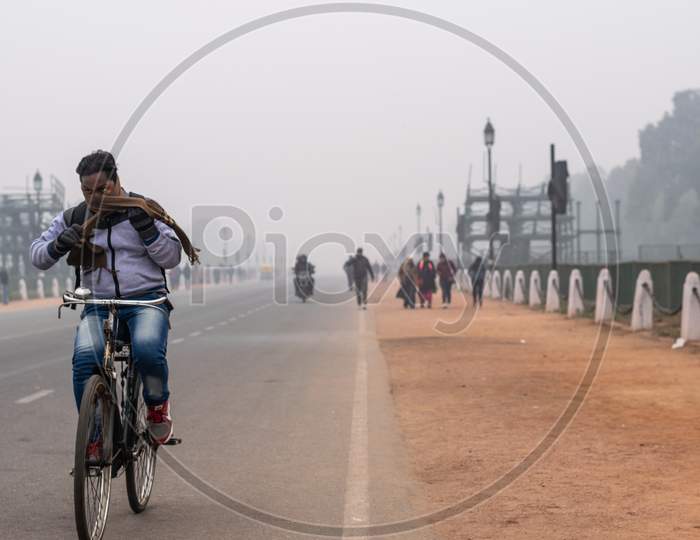 A man wearing muffler and other winter wears and riding bicycle in the foggy evening during winters in Delhi NCR