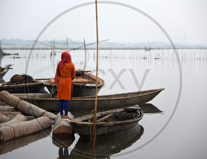 A Woman Waiting Stand On A Floating Wood As Her Husband Fishing In Beki River, In Barpeta District Of Assam