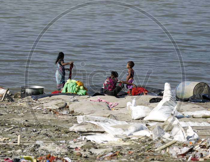 A Woman Washing Clothes In The Brahmaputra River As Her Children Waiting, In Guwahati