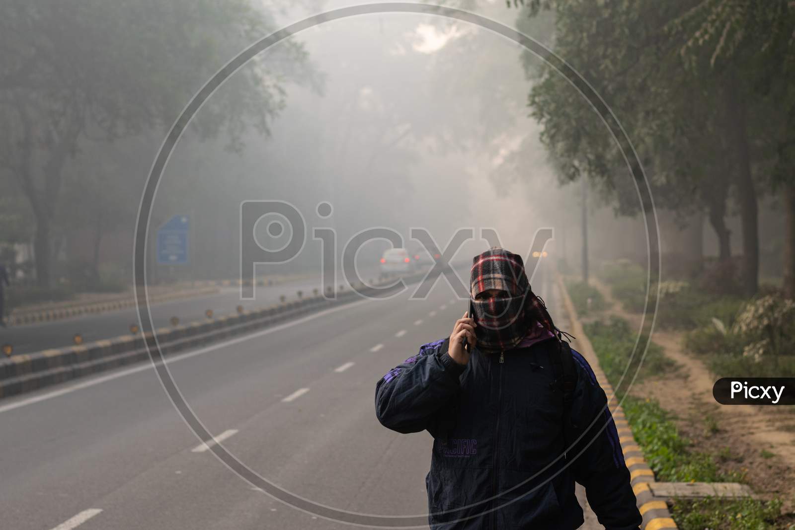 A man covering his face with muffler and wearing winter wears in the foggy morning during winters in Delhi