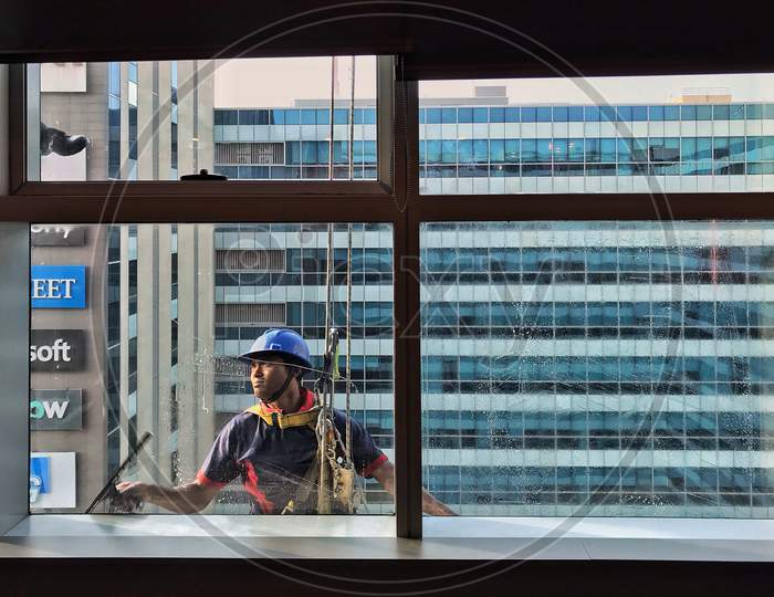 A person cleaning Window glass from outside using protective gear and ropes