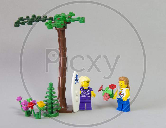 Florianopolis, Brazil. September 19, 2020: Long Haired Boy Minifigure Giving A Bouquet Of Flowers To His Surfer Girlfriend In The Garden On White Background. Valentine'S Day. Selective Focus.
