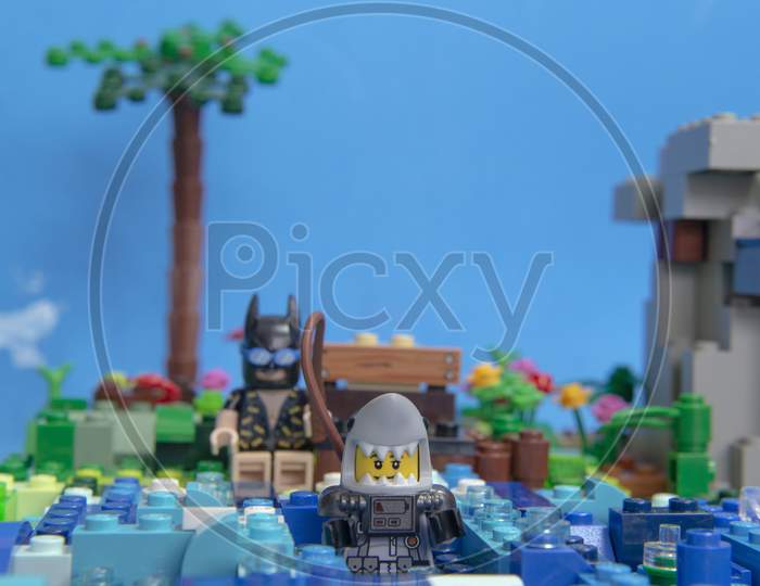 Florianopolis, Brazil. September 20, 2020: Batman Minifigure Sitting On A Wooden Bench On Shore Of Sea Fishing For A Shark. Super Heroes Also Have Time To Relax And Take It Easy.
