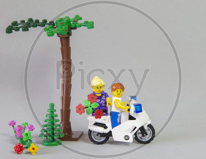 Florianopolis, Brazil. September 19, 2020: Minifigure Of Man Riding A Motorcycle With His Girlfriend On The Rump Holding A Bouquet Of Flowers On White Background. Valentine'S Day. Selective Focus.