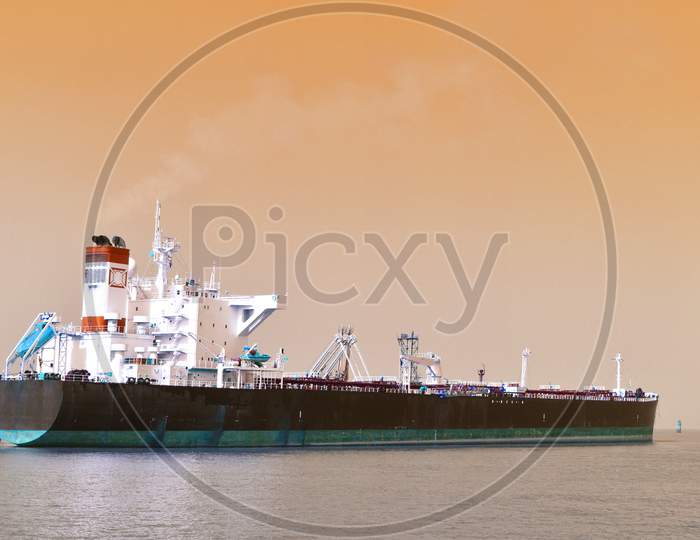 A Merchant Ship Standing In A Vast Ocean Under Beautiful Orange Sky