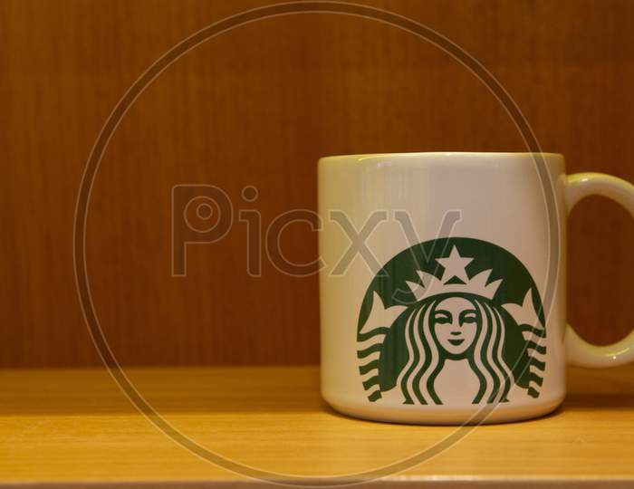 Florianopolis, Brazil. September 14, 2020: Porcelain Mug Of Starbucks On A Wooden Bench And Yellowish Lighting. Copy Space. Starbucks Is A Coffee Shop Known And Appreciated Worldwide.
